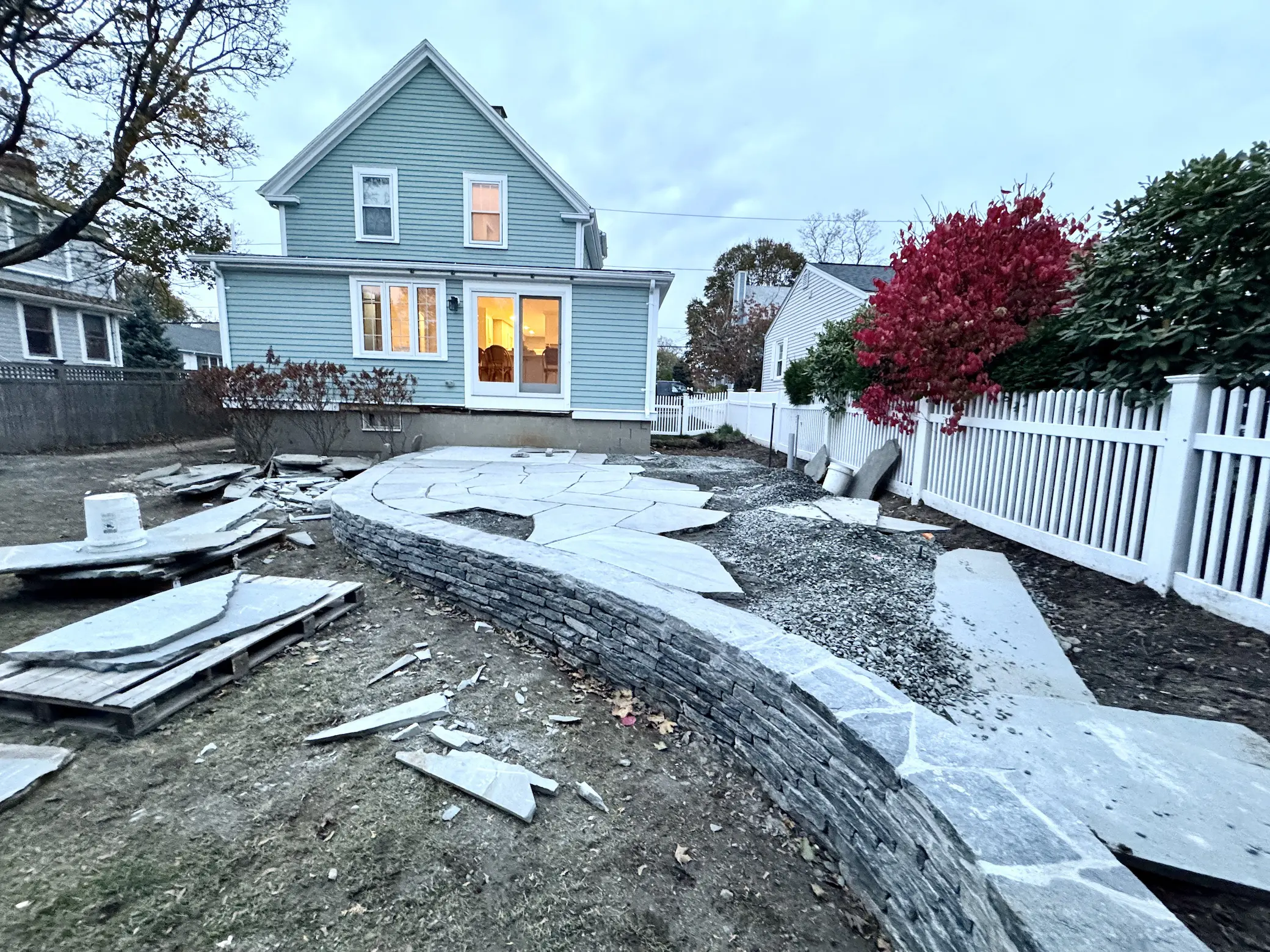 Backyard stone patio under construction with curved retaining wall hardscaping by Lasana's Landscaping